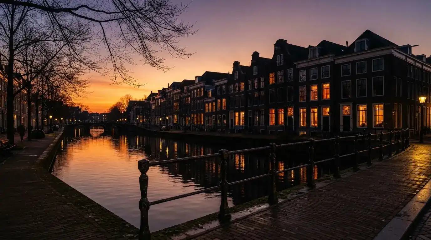 Een silhouet van kantoorgebouwen aan een Nederlandse gracht bij zonsondergang, met verlichte ramen langs het water.